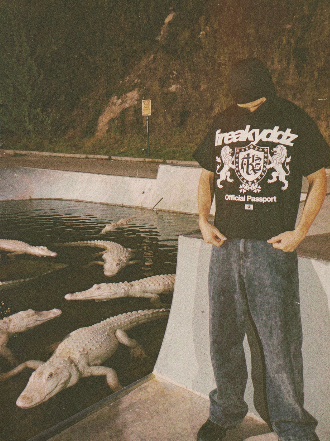 Modelo con el rostro cubierto y camiseta FREAKYDDZ junto a un estanque con caimanes de noche